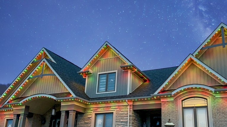 A house is lit up for entertaining with alternating green, yellow, and red Gemstone Lights permanent outdoor LED lighting.