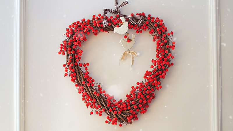 A heart-shaped wreath made of vines and red berries hanging on an exterior door.