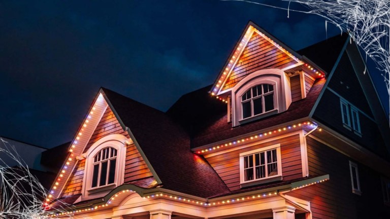 A 2 story house lit up with alternating groups of orange and white lights. There are cobwebs in the corners of the photo.