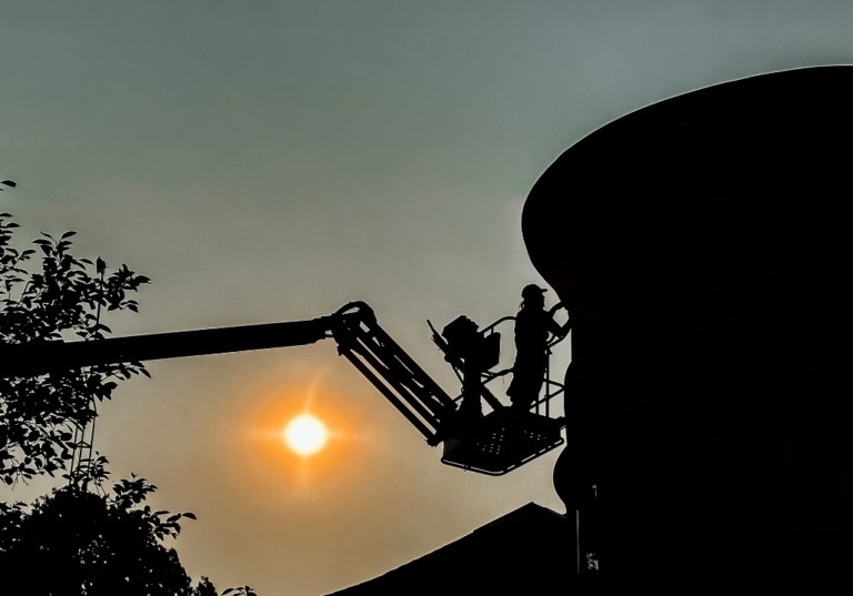 A lift platform with a man standing on it installing LED lights to a high, rounded wall structure with the sun setting in the background.