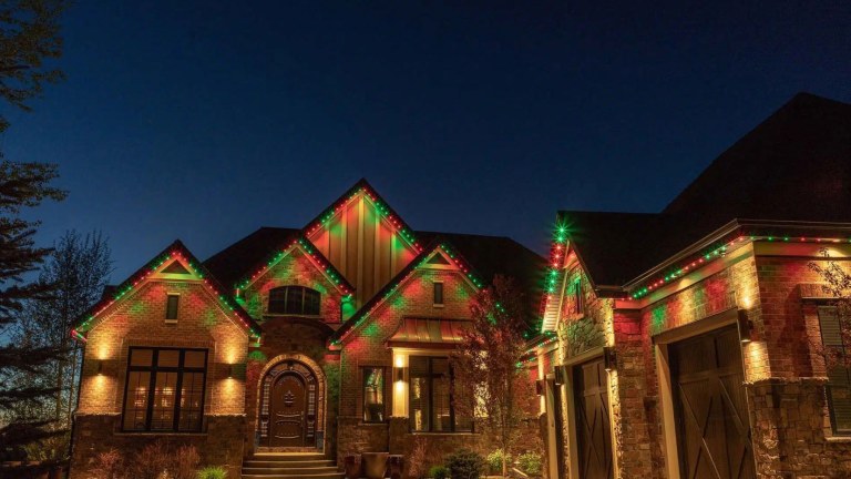 A two-story home and garage lit up with gemstone lights in red and green on all the roof lines