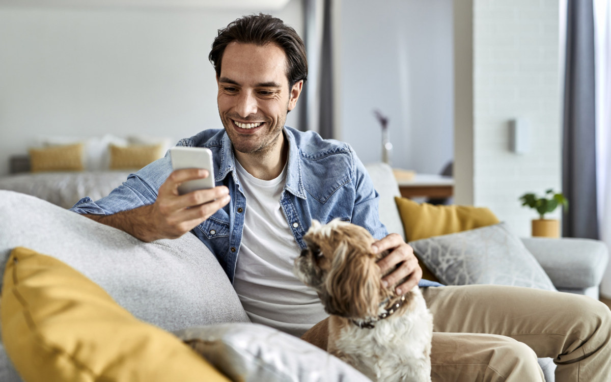 Man using his phone while sitting on a couch with his dog.