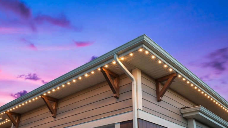 The corner of a house lit up with white Gemstone Lights Permanent outdoor LED lights. The sky in the background is purple and blue.