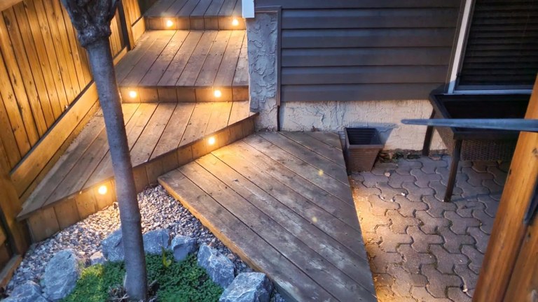 Gemstone lights shown installed on the front face of some curved wooden deck stairs